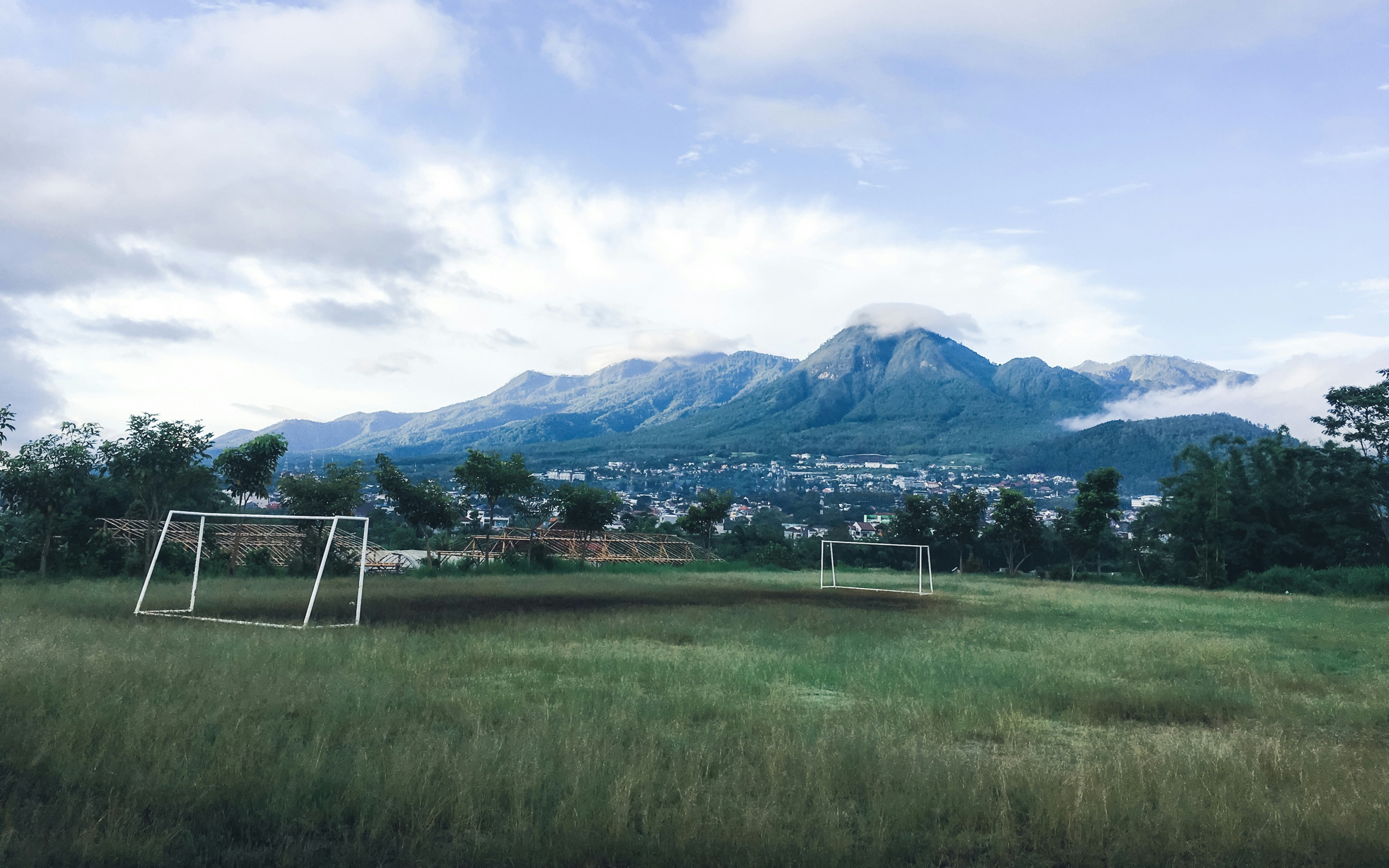 An empty grass soccer field with two goal frames and mountains in the distance.