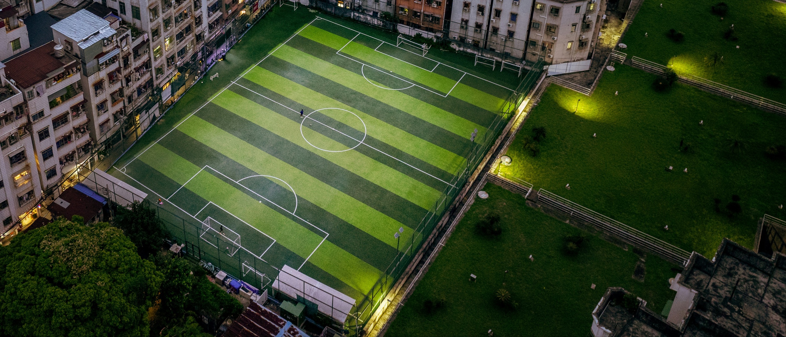 An illuminated soccer field beside apartment buildings at night.